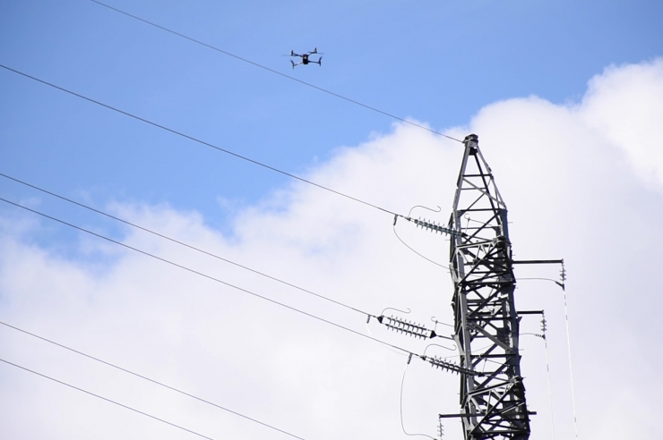 Un dron al costat d'una torre d'alta tensió.